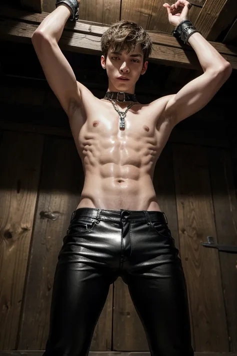 skinny young man chained to the ceiling of a dungeon by his wrists wearing leather pants shirtless oiled up