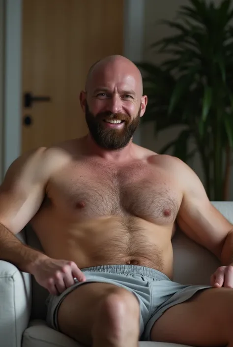 a man of 30, tall and strong, ((well-endowed)) bald with beard, sitting on the couch, wearing only thin fabric shorts, your excitement makes volume and marks something bulging in your shorts. he is shirtless. he is clearly sexually aroused.