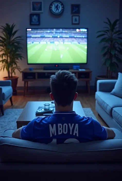 A Chelsea fan wearing a Chelsea shirt written MBOYA watching a Chelsea match in a living room 