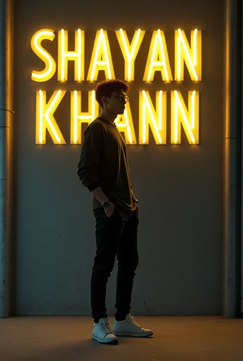 sneakers, he looks ahead. The background features "SHAYAN KHANN" in big and capital yellow neon light fonts on the dark grey wall