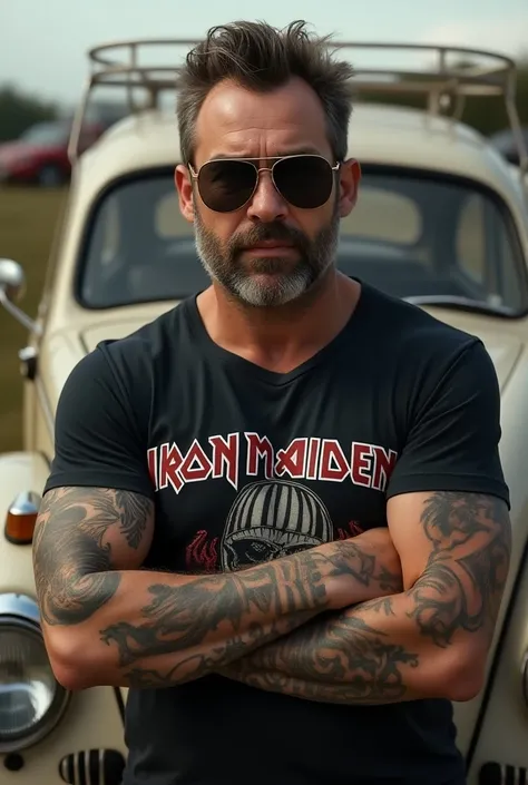 Man with a beard & short hair lower arm tattoos wearing iron maiden t shirt & sunglasses valkswagon beetle on background 