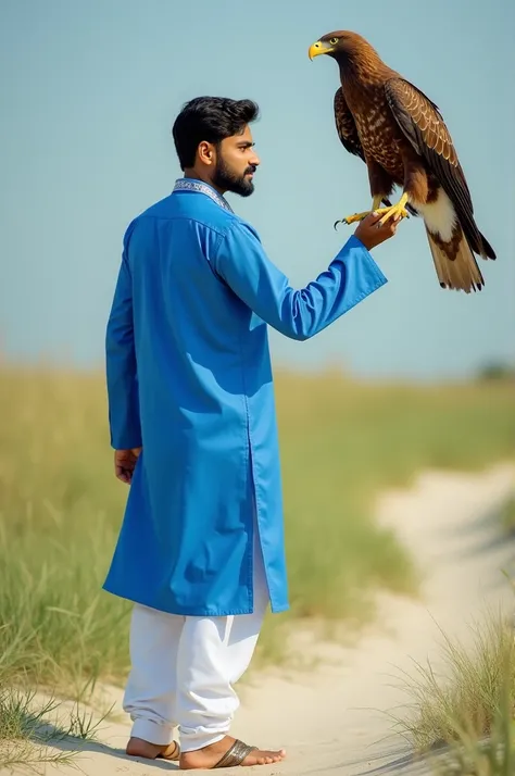 A 23 years old man is walking on a grassy beach wearing blue panjabi and white pajama. There is a eagle sitting on his hand. Capture is from backside.