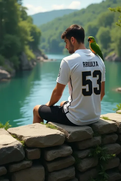 A 23 years aged brown color man is sat  on a dense riverside damn which is made of blocks. The man is  wearing a black pant and a real madrid jersey  of no 53  Named Profullya. There is a green parrot sitting on his shoulder. Capture is from backside witho...