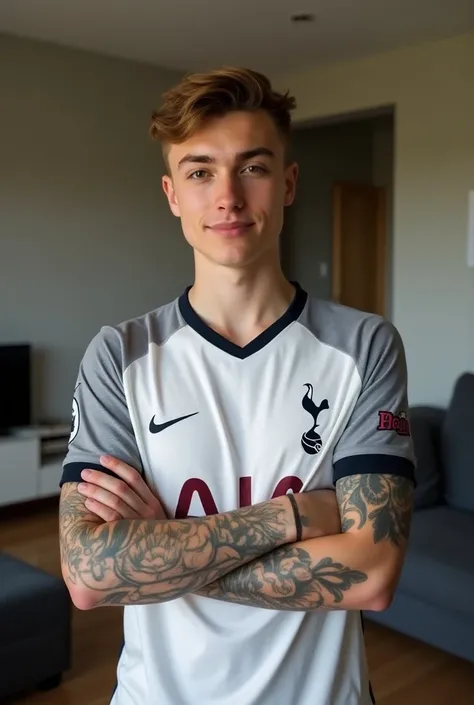 A 20 year old boy, with tattoos on their arms, Tottenham jersey , in the living room of his house posing for the photo 