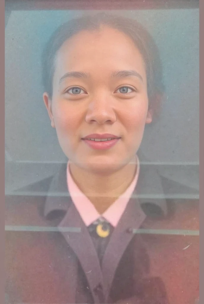 A portrait photograph of a young woman with a calm expression and slight smile. She has a round face, fair skin, and dark hair pulled back, revealing her facial features clearly. She is wearing a uniform-style outfit, including a buttoned jacket with a pal...