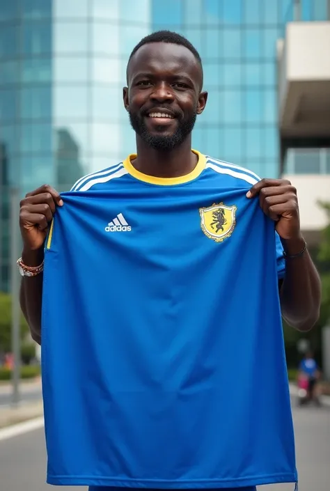 reality picture of a Tanzanian Man who wearing Yanĝa Sports club Jersey standing in front of the mall then holding blue big cloth billboard with both hands written 
"KIBAHA SHOPPING MALL
OPENING ON 7th December,2024"