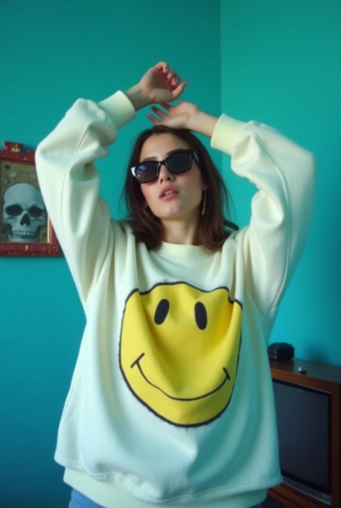 The image is a still from a music video. It shows a young  sexy woman wearing a white sweatshirt with a yellow smiley face on it. She is standing in front of a blue wall with a picture frame and a TV on it, with a skull on top of the TV. The woman is weari...