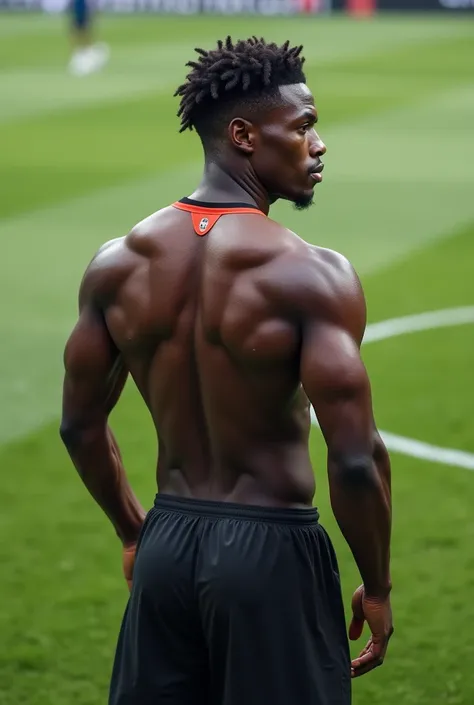 Joueur noir de peau, levé dos tourné sur un terrain de foot, en maillot (non floqué).