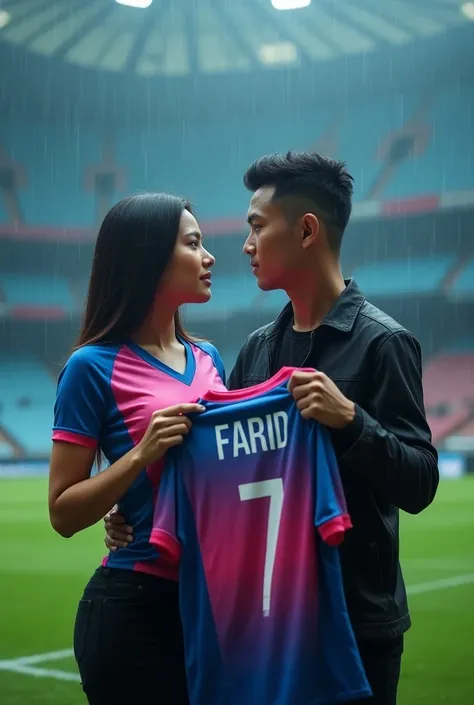 Photo of blue pink,wears a tight ball shirt her milk looks prominent  ,  next to an Indonesian man with neatly cropped hair wearing a black Jacket, they both look in front of the camera .  holding a football shirt that says “FARID” Number 7.  She stands on...