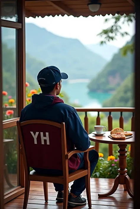 A 26-year-old Indonesian man wears a navy blue hat and a navy blue maroon jacket with the inscription YH, sitting in a chair looking at the mountain on the porch of a second-floor wooden house in the morning after the rain , Nearby there is warm coffee smo...