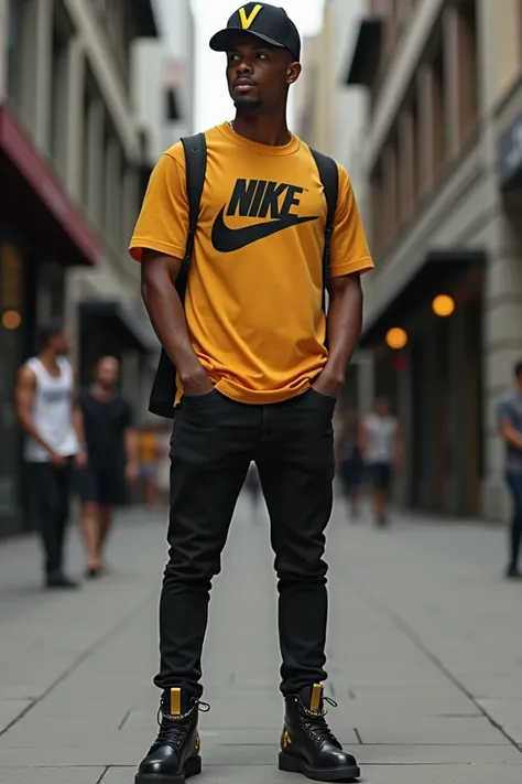  A man dressed in a black cap with a V in the center in yellow, a mustard t-shirt with the Nike logo in black ,  black skinny jeans and black ankle boots with gold details  