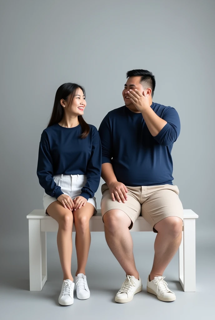 "Create a realistic couple portrait of a Thai pair in a casual pre-wedding photoshoot. Both are wearing matching outfits with navy blue long-sleeve tops and white sneakers. The woman has a cheerful smile, sitting on a white bench, wearing white high-waist ...