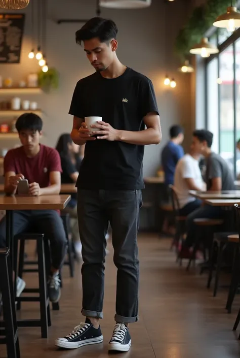 A handsome and sweet young man from Indonesia wearing a black t-shirt with bigreds black jeans and black Converse shoes is lowering his head looking at a coffee cup on the table in an aesthetic coffee shop with the atmosphere of some visitors looking reali...