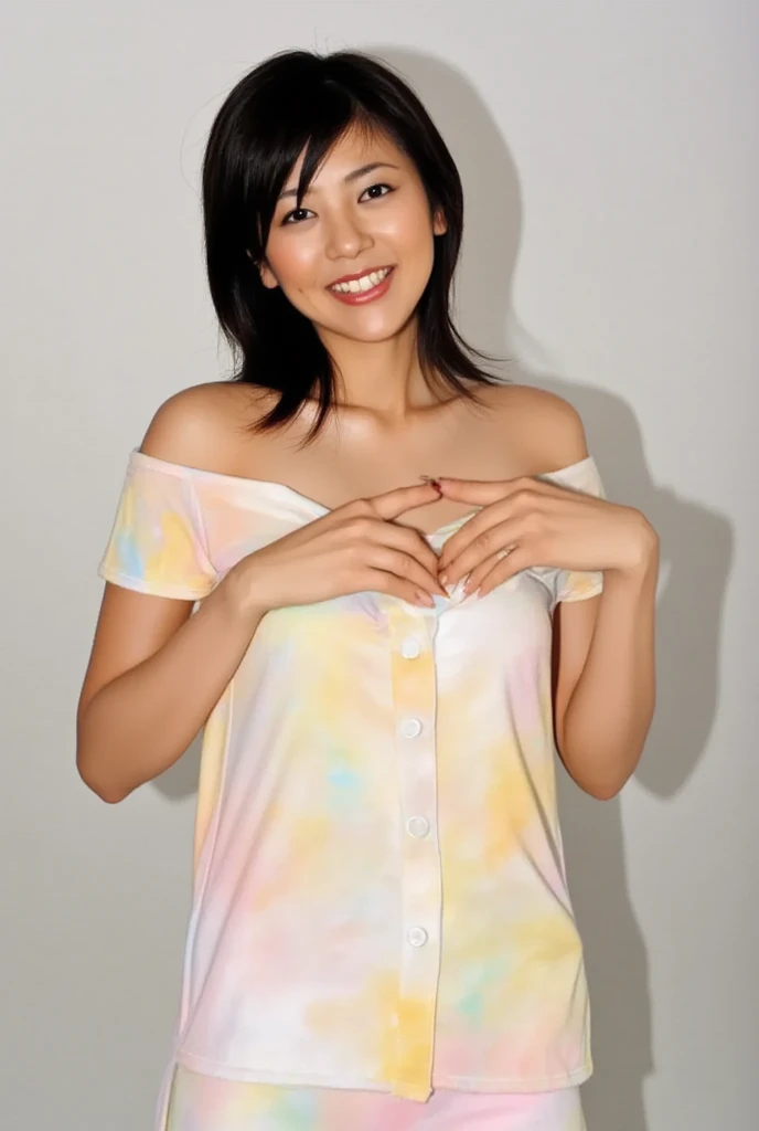 A smiling woman poses alone wearing off-the-shoulder pajamas in pastel colors that convey warmth simply by touching them softly and softly, making a firm, large heart shape with both hands, and holding them in front of her chest, View above collarbone、The ...