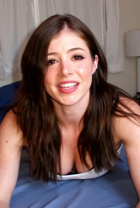 Amateur selfie of a young Chrissy lying on her stomach in her bed. She has long, wavy hair that is blowing in the wind. She is smiling and looking directly at the camera. The woman is wearing a white tank top displaying her cleavage. The background is blur...