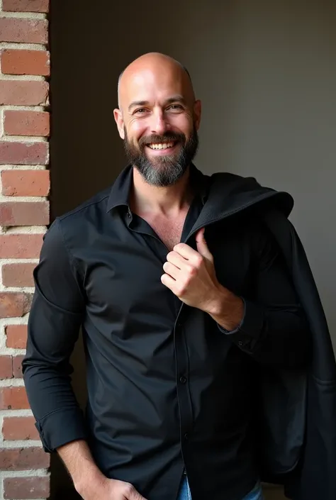  The image shows a bald man with a short and well-groomed beard ,  wearing a black dress shirt open around the collar .  He is positioned next to a brick wall and holds a coat over his right shoulder, conveying a relaxed and confident posture .  He smiles ...