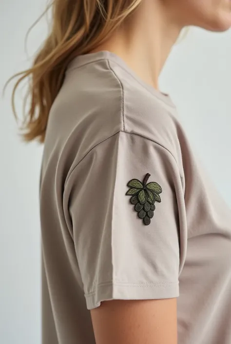 A taupe t-shirt embroidered in a size of 5cm x 5cm and a grape in black and green ,  on the upper right edge  . 
