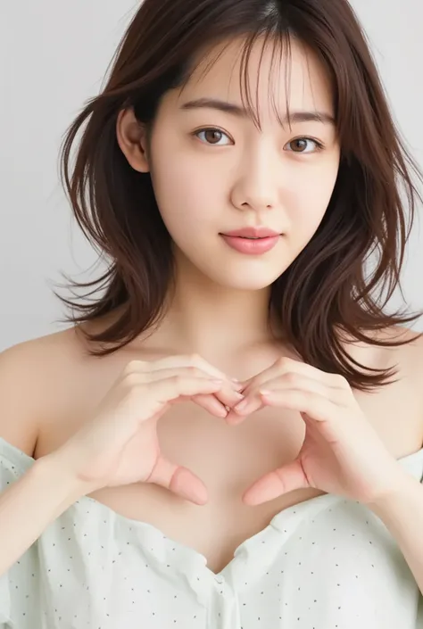 A smiling woman poses alone wearing off-the-shoulder pajamas in pastel colors that convey warmth simply by touching them softly and softly, making a firm, large heart shape with both hands, and holding them in front of her chest, View above collarbone、The ...