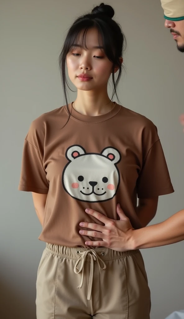 Headshot of a Japanese woman wearing a brown t-shirt with a cute pattern and chinos standing facing the front and stretching her chest with her hands behind her back and getting her chest rubbed from behind by a man wearing a blindfold