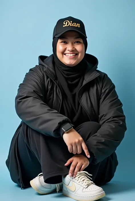  Photo Dian ladydian is sitting playfully against a light blue background .  She wears a modern and neat hijab wears a black base ball hat with the name  "DIAN"  written in metallic gold .  Dian looks current , wearing a black t-shirt hodie jacket , black ...