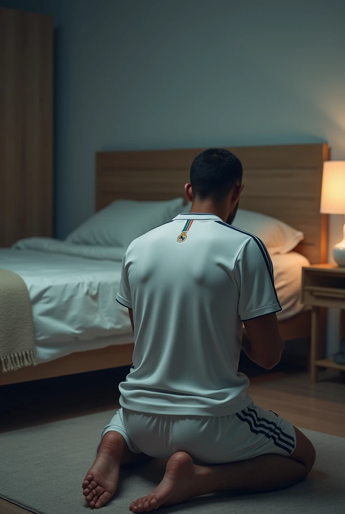  on knees, praying in front of his bed wearing a white Real Madrid shirt