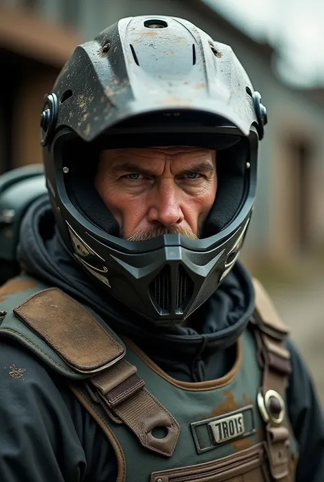 A man wearing a motocross helmet and an armoured vest looks at the camera 