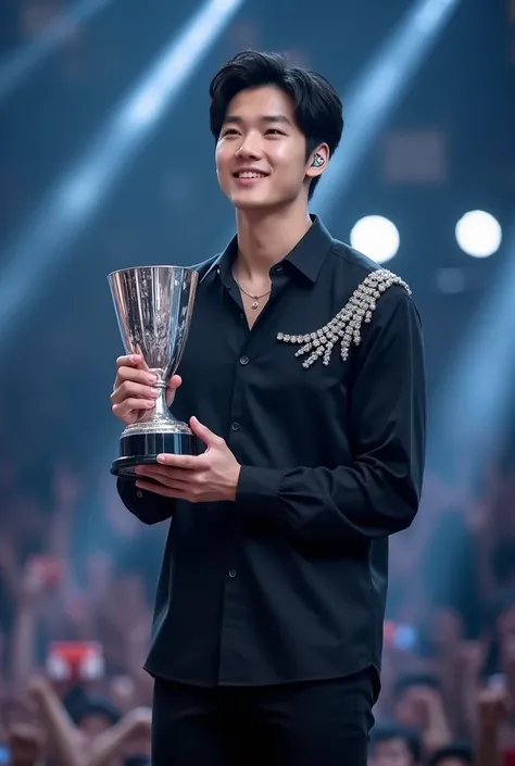 A male kpop idol wearing Black shirt with silver jewellery attached on the shoulder only and Giving Speech on stage  with a silver trophy in his hand