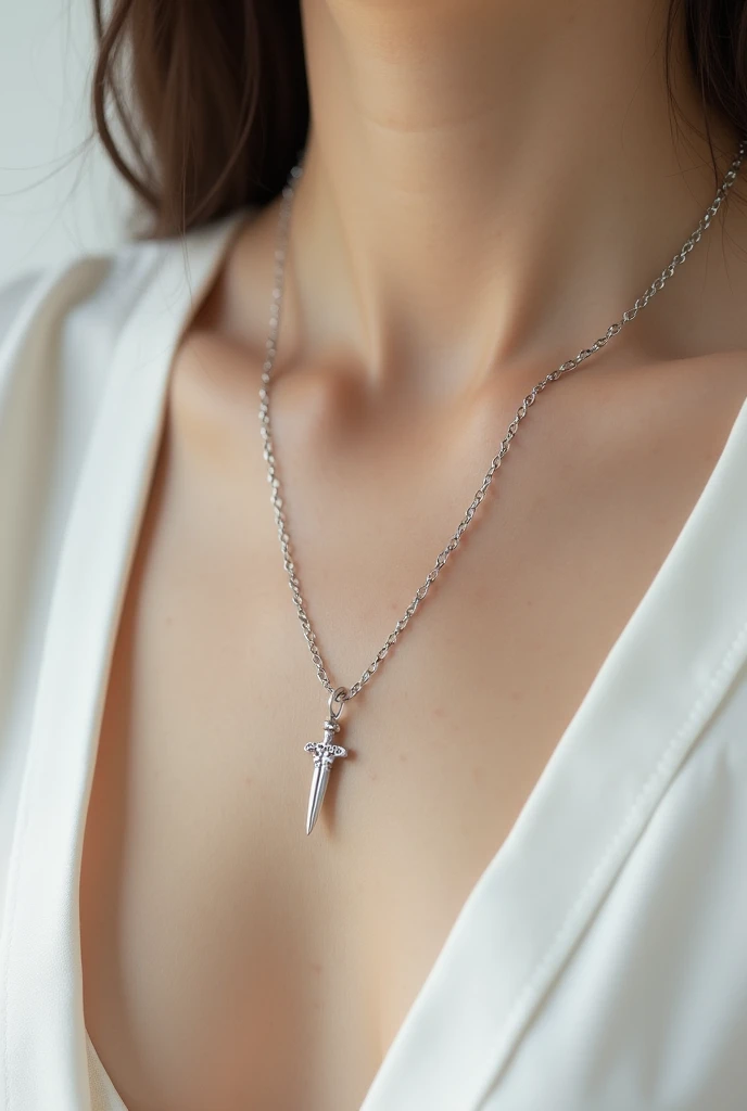 A small, thin, silver necklace with a tiny dagger on a white chest