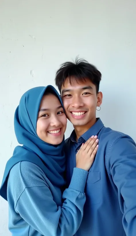 two Indonesian teenage couple selfie, girl wearing blue sweater and hijab, guy wearing blue shirt, tall guy, short girl, white wall behind they