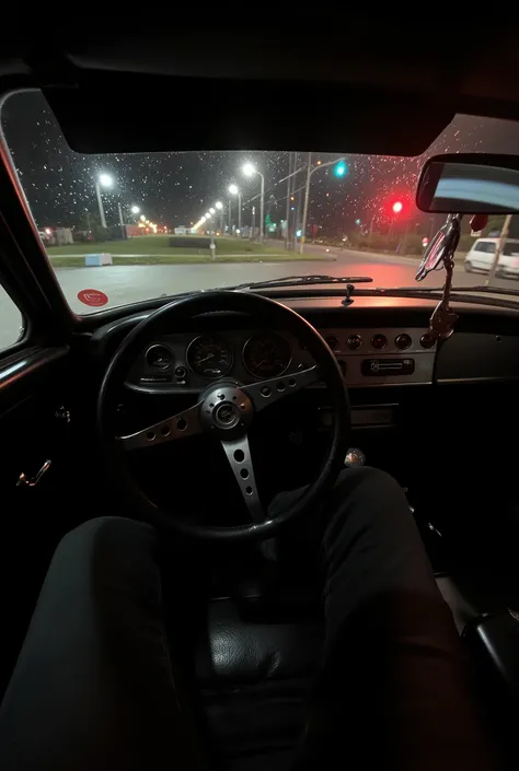 A nighttime drivers perspective directly facing the sporty and minimalist steering wheel of a vintage car, entirely black without any letters or brand symbols. The car is stationary at a red traffic light in Brazil, with no other vehicles ahead. Small rain...