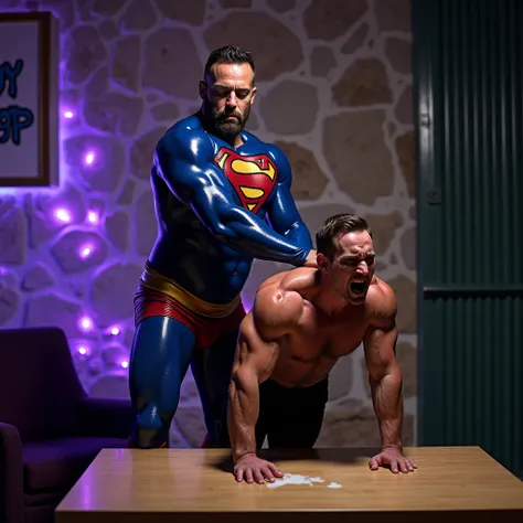 A dramatic sex scene featuring two men in an indoor setting with a stone wall background. The 55 year old Canadian bodybuilder on the left, dressed in a shiny blue rubber-like costume resembling superman attire with red and yellow accents, presses behind h...