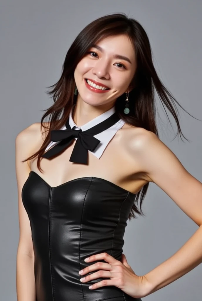 The image is a portrait of a young woman posing in a black strapless leather leotard. She is standing with her body slightly turned to the side, with one hand on her hip and the other resting on her head. The woman has long dark hair that is styled in loos...