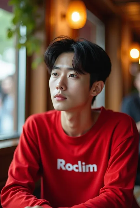 Beautiful white young korean man sitting at the cafe, wearing tops red with names Rochim  on its.