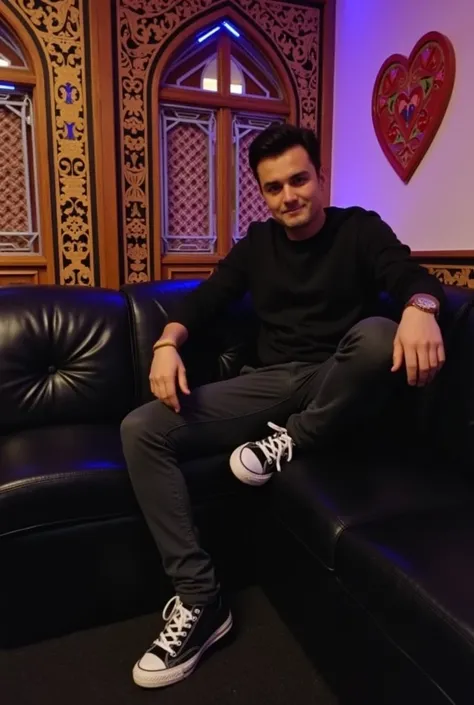 The image shows a person sitting on a black couch in a room decorated with intricate wooden carvings and colorful lighting. The background features a heart-shaped design on the wall, adding a romantic touch to the setting.