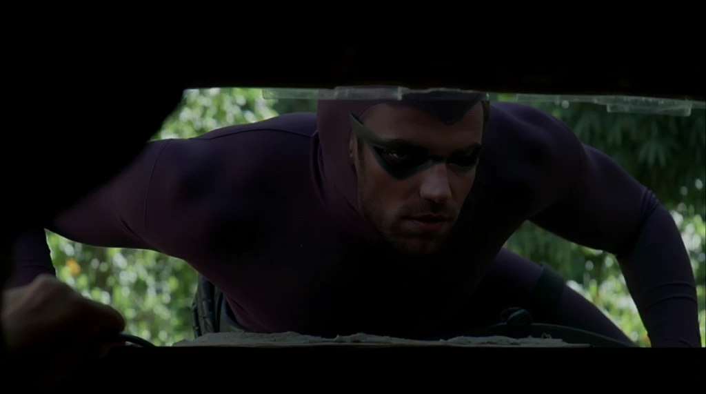 Zane Phillips, a masked superhero in a dark and smoky elevator at night. Clad in a sleek, purple body-hugging lycra costume with a matte finish, his defined muscles and muscular arms are on full display. The costume features a purple collant that glides se...