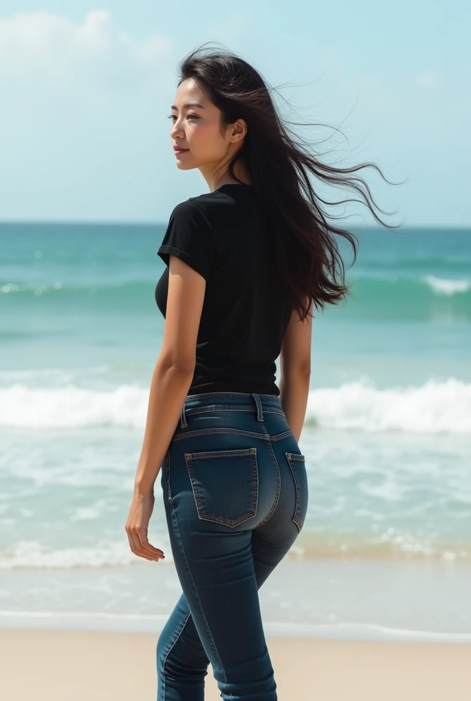 an adult woman who is not too fat, with long black hair, wearing a black t-shirt and dark blue jeans, is walking along the beach