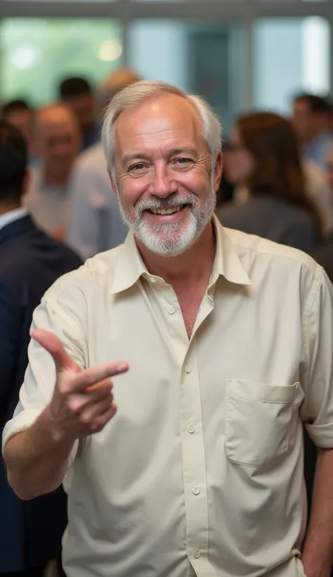 "A smiling man with a white beard wearing a light-colored dress shirt. He is in an environment with a blurred background, possibly at an event or institutional setting. The man is making an 'L' gesture with his hand toward the camera. Behind him, partially...