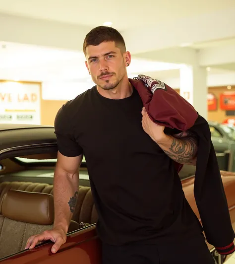  The image shows a man wearing a tight black t-shirt , leaning on a car with a brown interior .  He holds a burgundy jacket over his right shoulder and wears a short, well-defined haircut.  His expression is serious but relaxed ,  with a slight inclination...