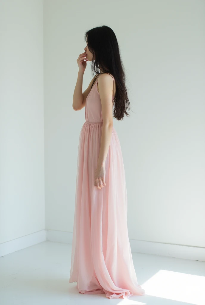 Dark-haired, long-haired woman posing in a white room is in profile covering her face with one hand, Skinny in a pink dress