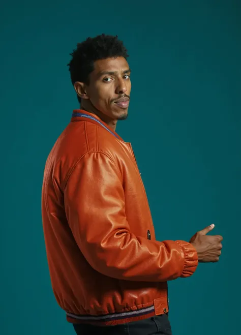 A dark-skinned man, approximately 25-35 years old, is featured in a studio portrait. He is positioned in a three-quarter profile view, slightly turned away from the camera and angled to his right.  He is wearing a rust-colored, leather bomber jacket with v...