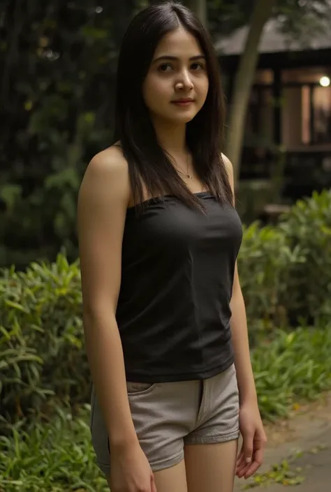 Young woman with medium skin tone and long dark hair, wearing a black sleeveless top and light gray shorts, standing in an outdoor setting at night with soft lighting in the background