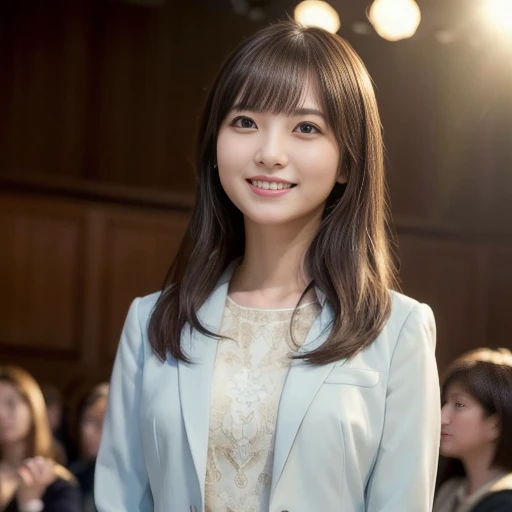 A woman emceeing a lecture, standing to the side of the stage, she is wearing a cream colored suit and skirt, captured from a frontal downward perspective, there are audience members sitting in the background, illuminated by warm lights, the surroundings a...