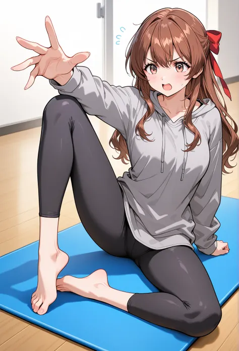 A woman with wavy brown hair and a red ribbon tied in a bow, wearing a loose gray sweatshirt and black leggings, sitting on a yoga mat with one leg extended and the other bent, her hands reaching toward her toes, expression determined.