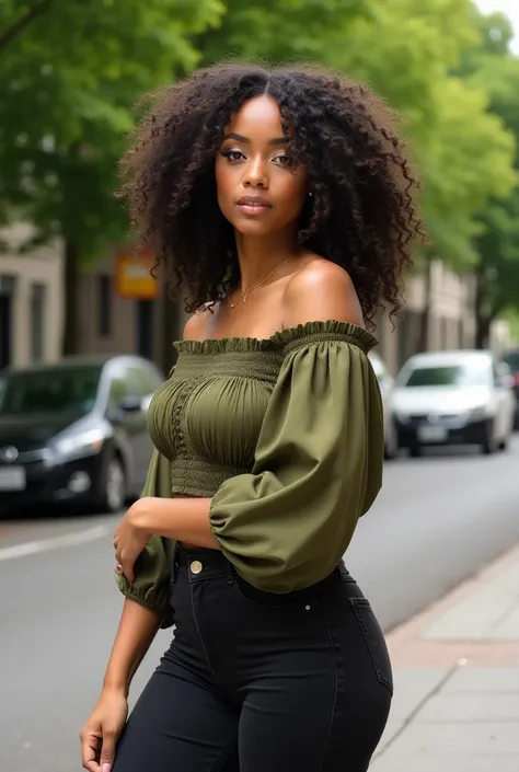 [A woman with large, voluminous curly hair is standing outdoors; she is wearing an olive green off-the-shoulder smocked crop top and black high-waisted jeans; her pose is confident and relaxed, projecting a stylish and self-assured mood; the background fea...