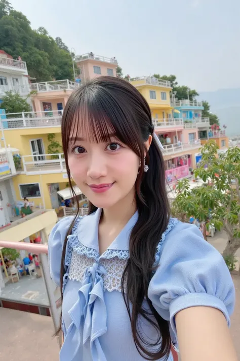 A cheerful young woman wearing a casual summer outfit stands on a viewpoint overlooking the vibrant, pastel-colored houses of Gamcheon Culture Village in Busan. She holds her camera, capturing the scenic beauty of this artistic hillside town.

