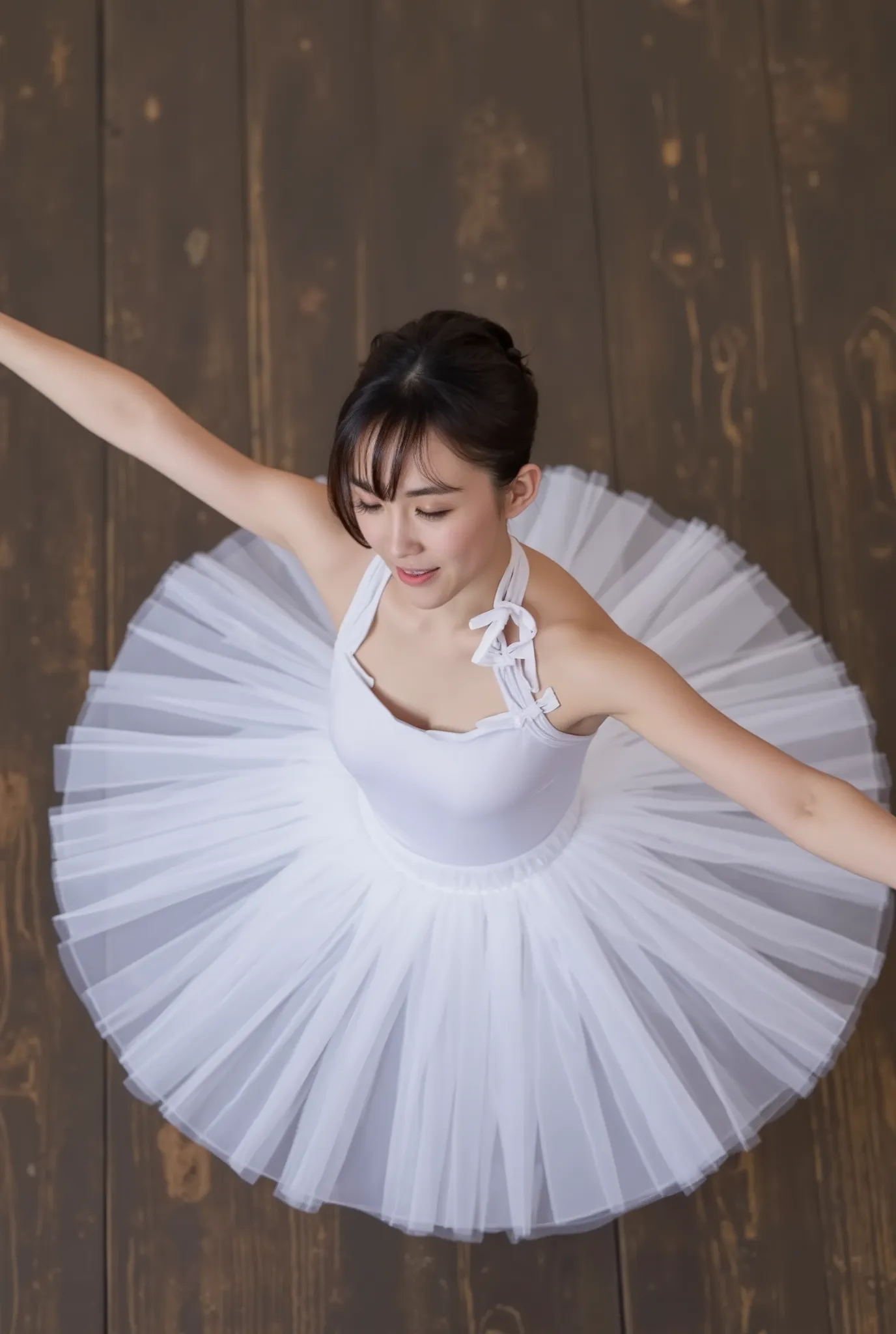 A high-resolution photograph of a ballet dancer captured mid-movement from an elevated angle. The dancer is a young woman with a fair complexion and straight black hair neatly styled into a bun. She wears a classic white ballet costume, featuring a fitted,...