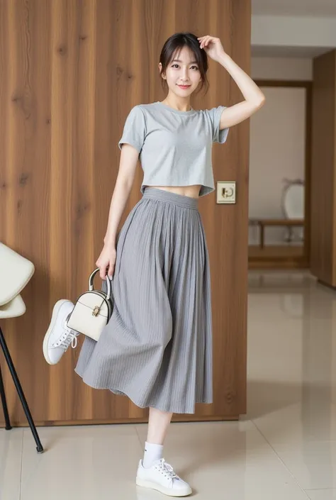 A fashionable asian woman standing in a contemporary indoor setting, wearing a grey pleated skirt and a light grey crop top, styled with white socks and white sneakers. She carries a small white handbag in one hand while playfully lifting one leg. A wooden...