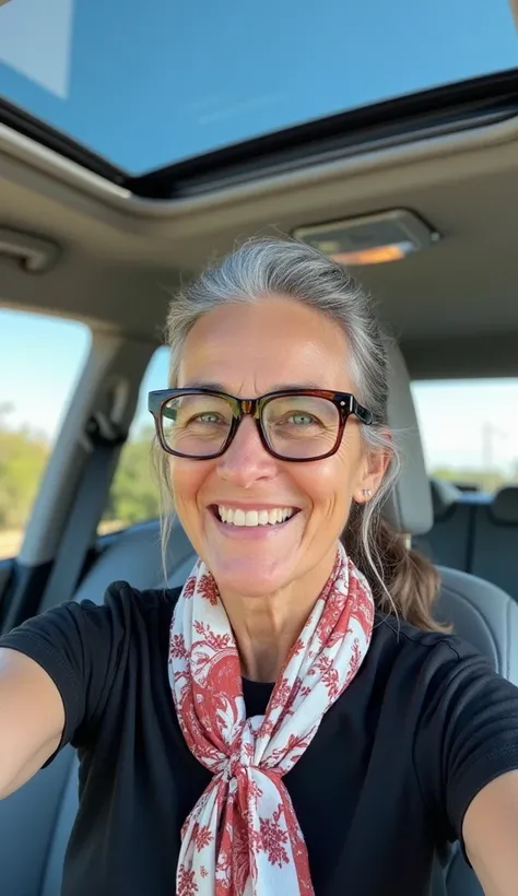  A fair-skinned woman , looking about 40 to 50 years old, smiles warmly at the camera while taking a selfie inside a modern car with an open sunroof. She has gray hair tied behind her and wears dark brown framed glasses.  your smile is wide , and she wears...