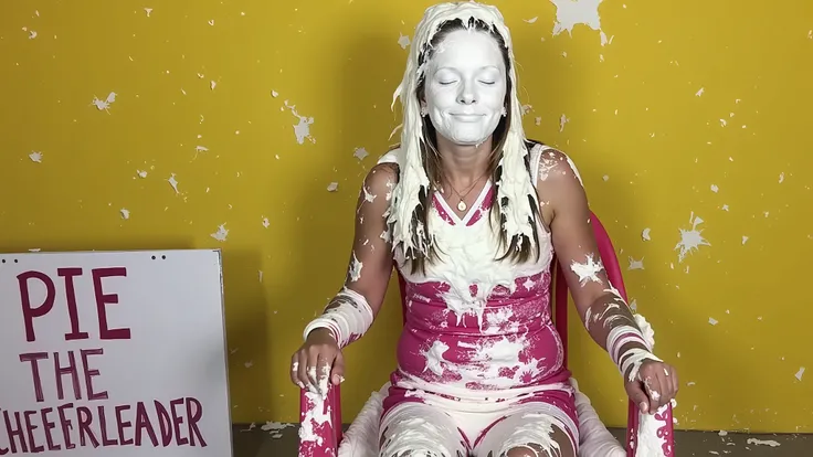 A beautiful 18-year-old girl wearing a cheerleader outfit sits in a plastic chair in a stall at a carnival.  There is a sign on the ground next to her with the words "PIE THE CHEERLEADER" written on it.   She has been pied several times and her entire face...