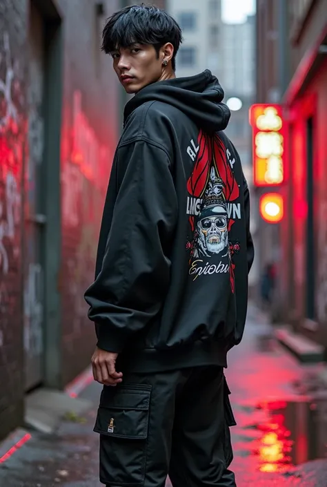 A confident korean male model showcasing an urban streetwear outfit in a gritty, industrial city environment. The outfit features a matte black oversized hoodie with bold, street-inspired graphic prints across the back and sleeves, with a large 'LANCE_CROW...